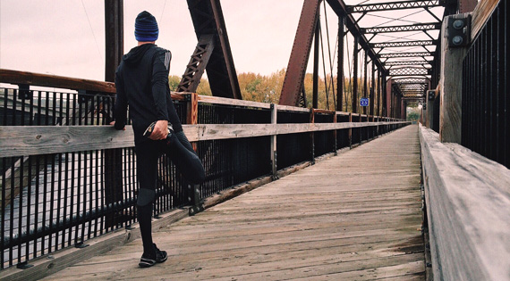 Homme en tenue de sport s'étirant sur un pont en bois.